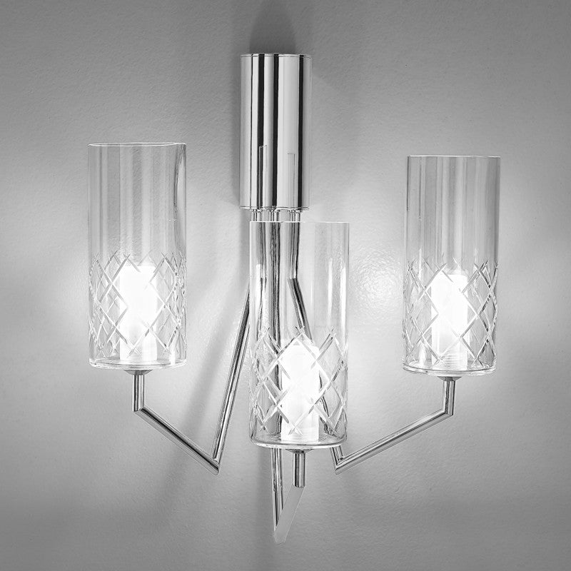 Bri-Bri Wall Light by Zaneen Shop - A fixture with a chrome finished-base, featuring three arms, holding transparent glass cylinder lights.